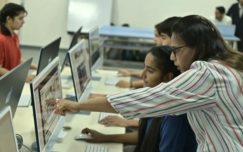 Students and teacher collaborating in a computer lab, discussing digital content.