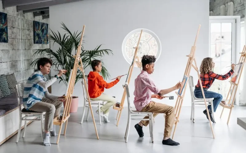 Young students focus on painting during an art class indoors, using easels.