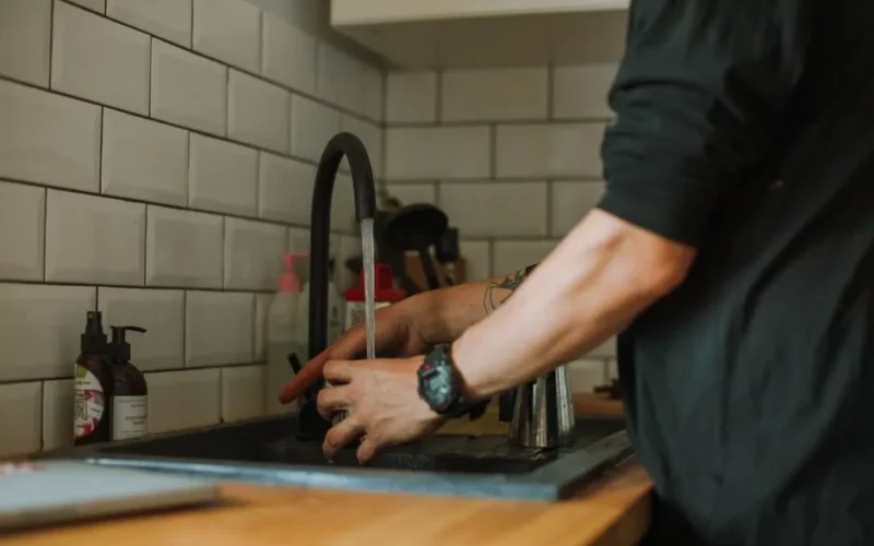 Close-up of a person washing hands at a sink with running water, wearing a wristwatch.