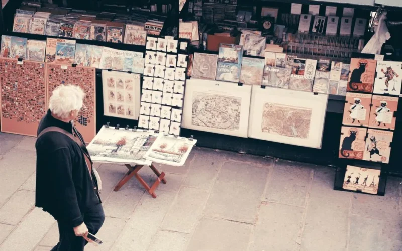 An elderly man browsing art prints at a street market in Paris. Urban and cultural scene.