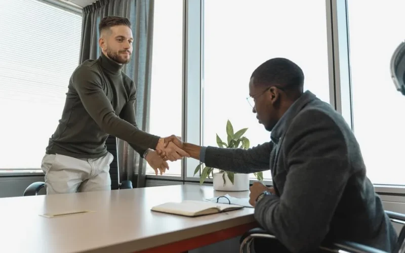 Two businessmen shaking hands in a modern office after a successful meeting or interview.