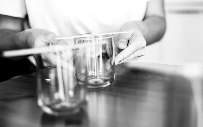 A close-up black and white photo of hands setting wicks in glass holders, emphasizing DIY crafting.
