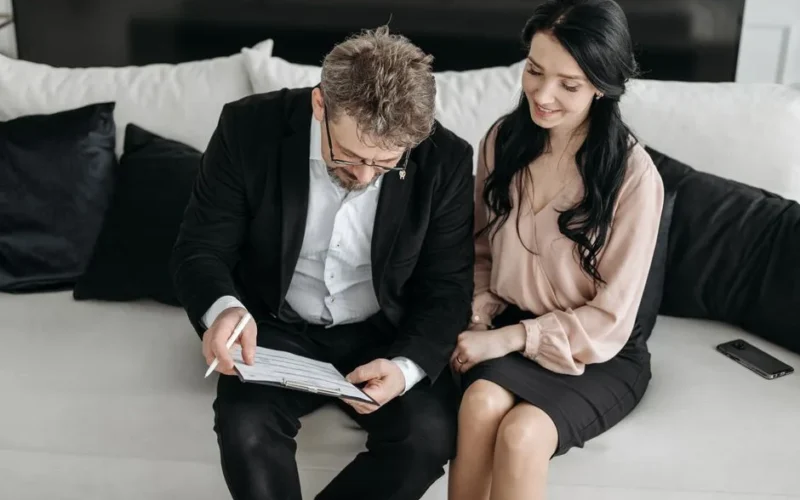 Business couple reviewing documents together on a couch, highlighting teamwork and success indoors.