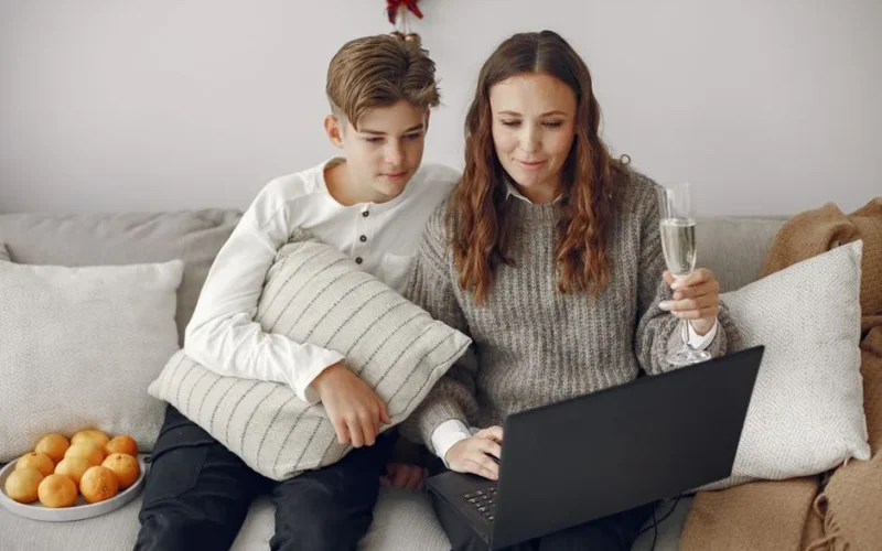 A mother and her teenage son sitting on a couch, shopping online using a laptop.