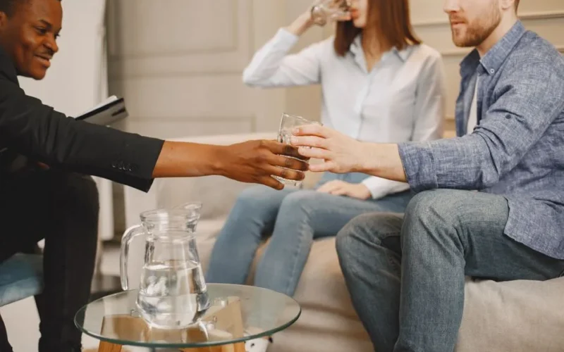 Therapist interacting with couple during counseling session indoors, sharing water.