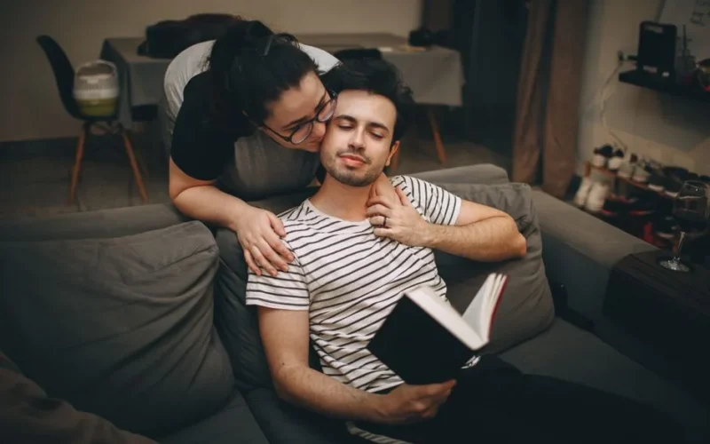 A couple enjoying a cozy moment indoors, reading on a sofa and embracing.