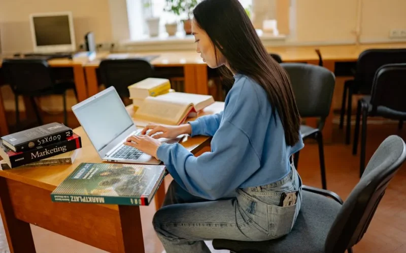 Focused woman typing on laptop, surrounded by books in a cozy study spot.