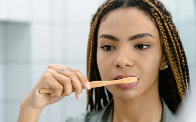 Close-up of a woman with braided hair brushing her teeth, highlighting oral hygiene.