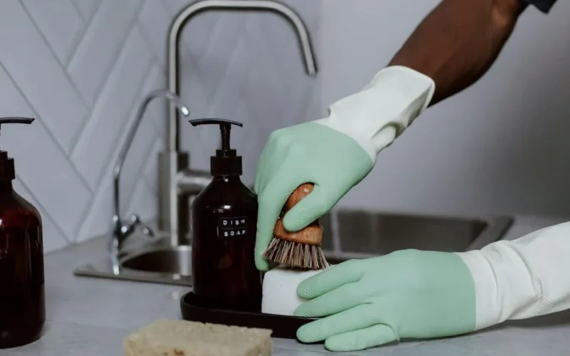 Hands in latex gloves washing dishes with soap at a kitchen sink.