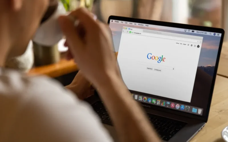 Close-up of an adult drinking coffee and browsing Google on a laptop indoors.