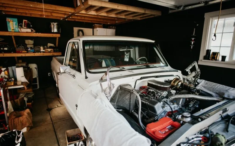 A vintage pickup truck undergoing engine repairs in a well-equipped home garage.