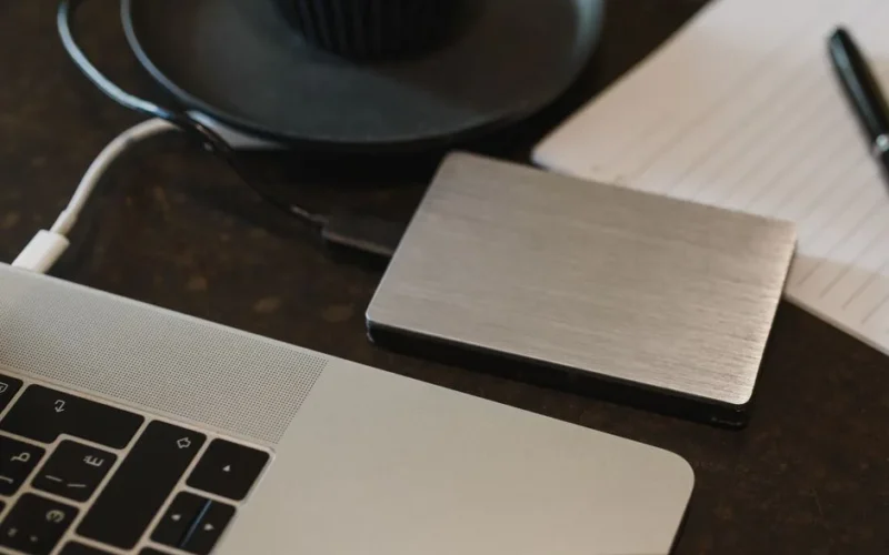 Closeup of an external hard drive connected to a laptop with a USB cable on a desk.