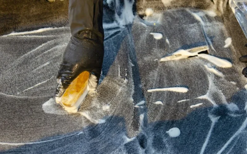 A detailed view of cleaning in progress, focusing on a gloved hand using a brush with detergent on a surface.
