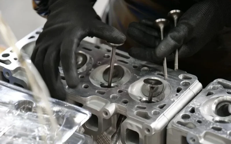 Close-up of mechanic's hands working on engine cylinder head assembly with valves.