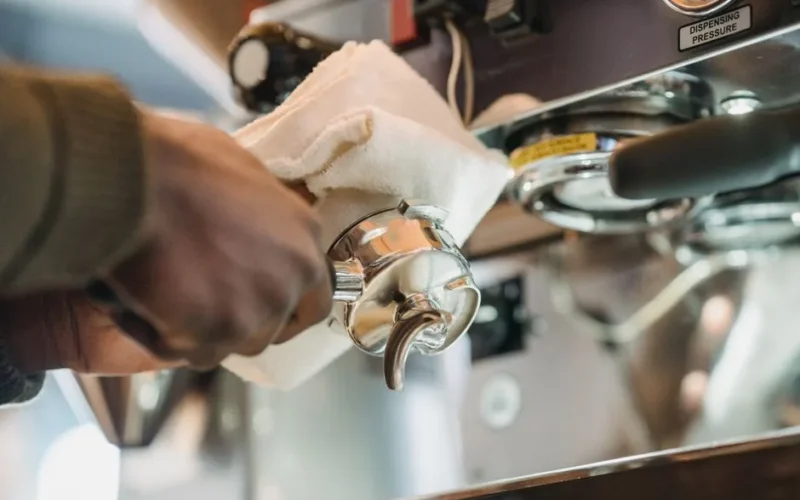 Close-up of barista cleaning a coffee machine portafilter with cloth for hygiene.