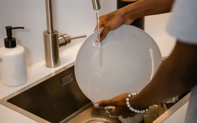 A close-up view of a person washing a plate in a modern kitchen sink with water running from the faucet.