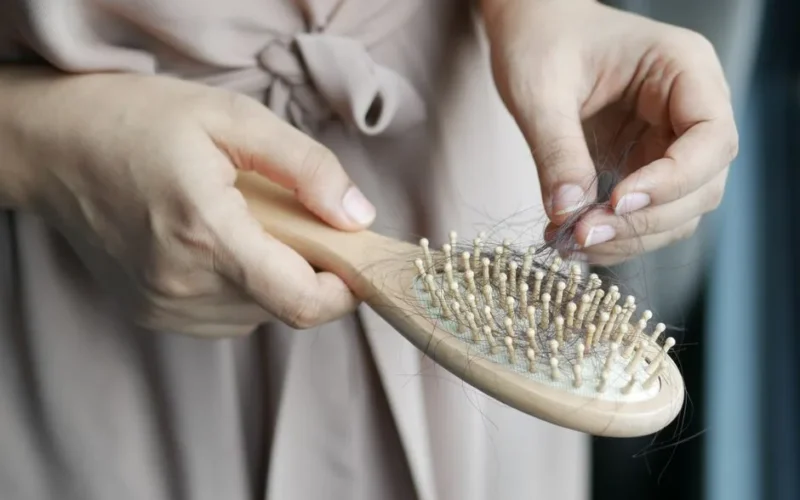 Close-up image of hands removing hair from a wooden brush, emphasizing daily hair care routine.