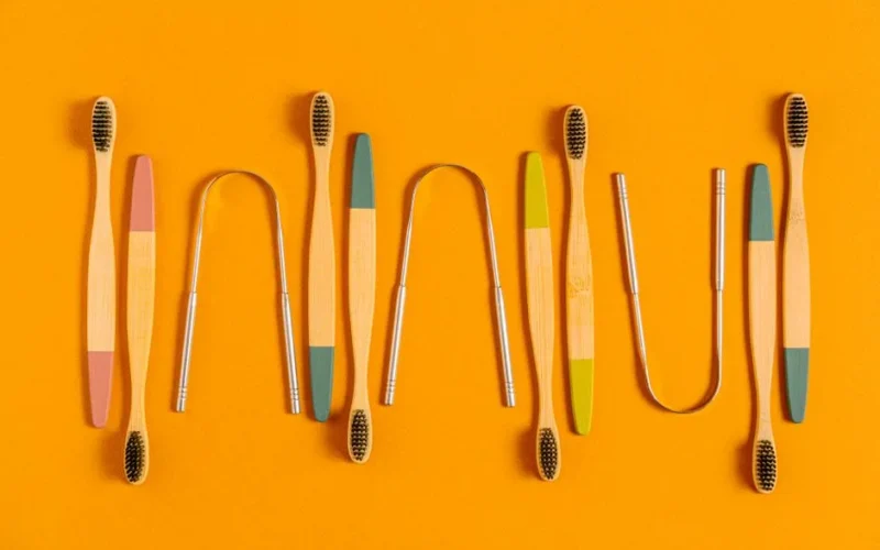 Stylish bamboo toothbrushes and tongue scrapers on a vibrant orange background, promoting sustainability.