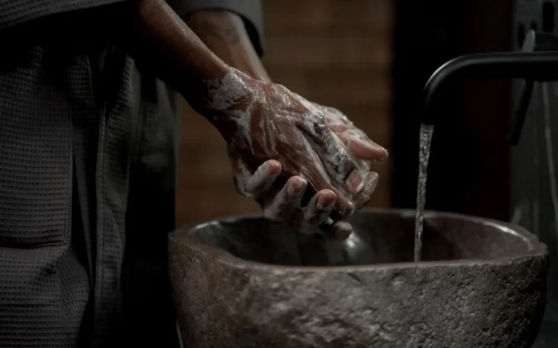 Man washing hands with soap in stone basin for hygiene and cleanliness.