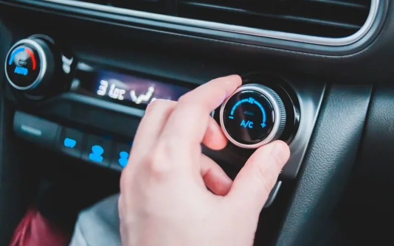 Crop anonymous person regulating temperature in car using controller on panel while sitting in car