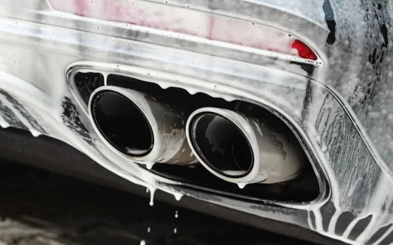Dual exhaust pipes covered in soap suds during a thorough car wash.
