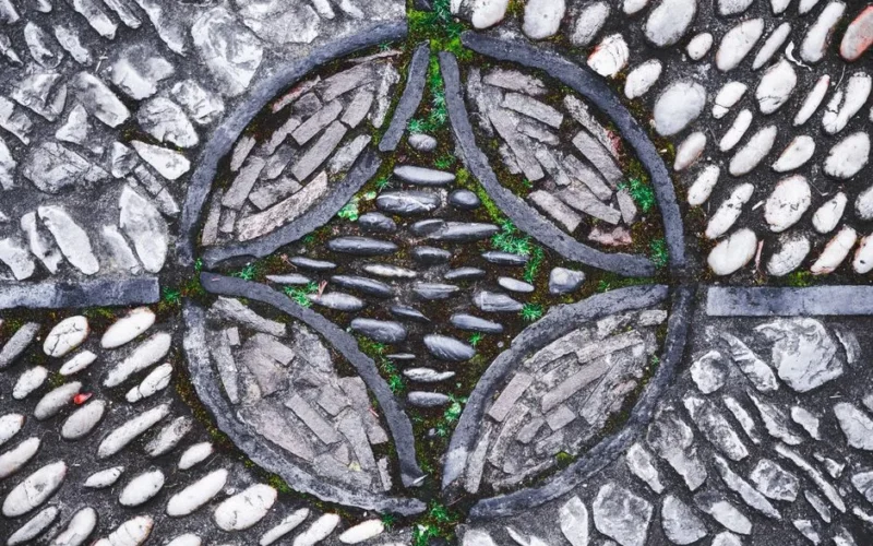 Top view of gray stone and cement paved footpaths and green grass breaking through cracks