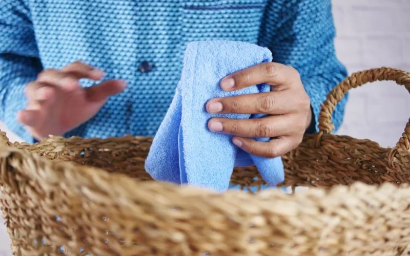 Close-up of hands placing a blue towel over a wicker basket. Ideal for laundry or home decor themes.