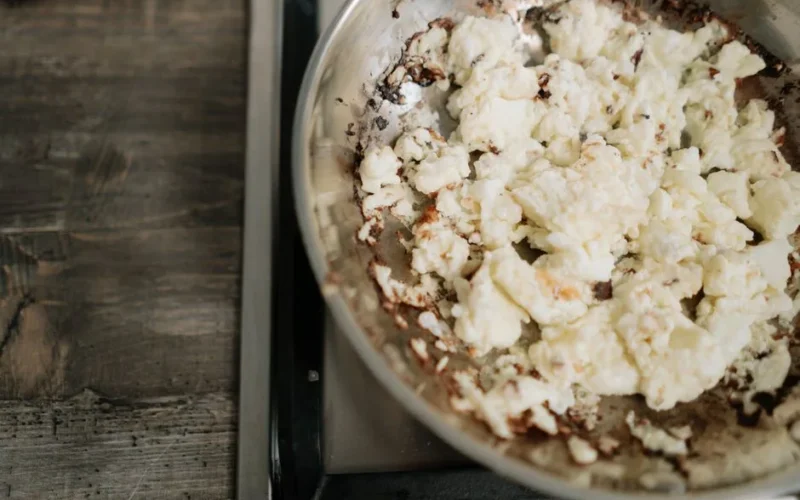 Overcooked scrambled eggs in a stainless steel skillet on a stove.