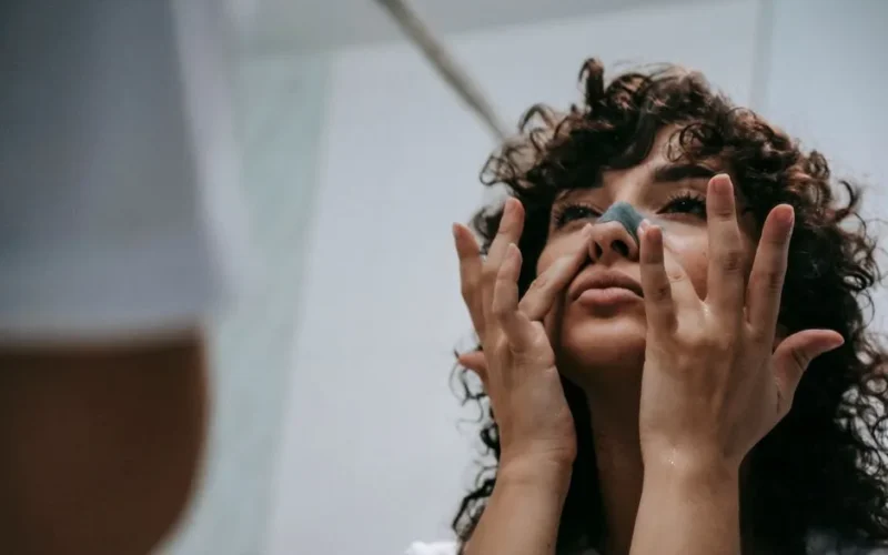 From below of young curly brunette standing in front of mirror and cleansing nose skin with cosmetic strip