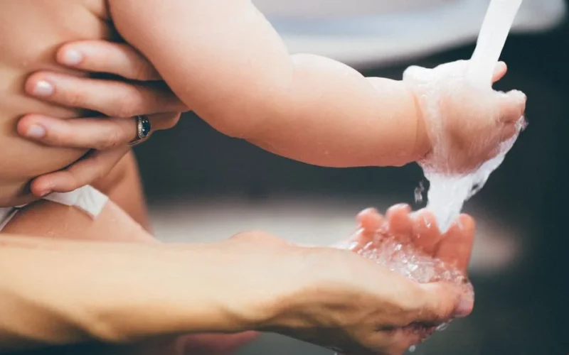 Heartwarming close-up of a parent gently washing a baby's hand under running water.
