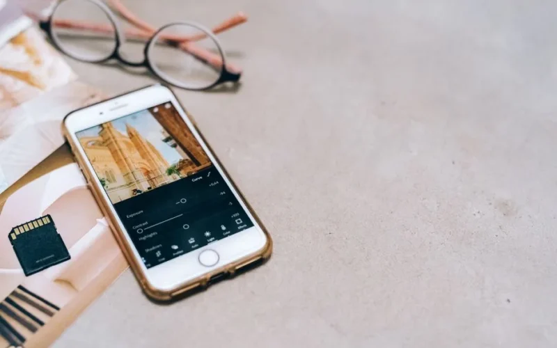 Smartphone displaying a photo editing app, next to a memory card and glasses on a table.