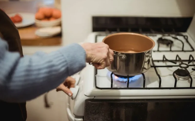 Crop anonymous female chef placing saucepan with clean water on burning gad stove while cooking in kitchen