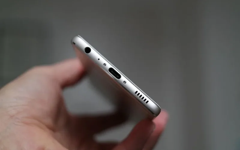 A close-up view of a person holding a smartphone, focusing on the charging port and headphone jack.