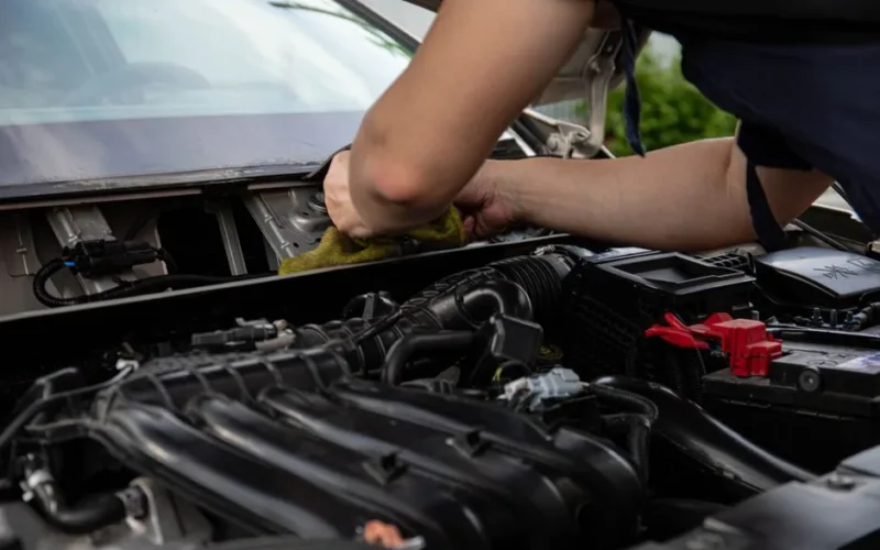 Close-up of a mechanic working on a car engine, showcasing hands and engine details.