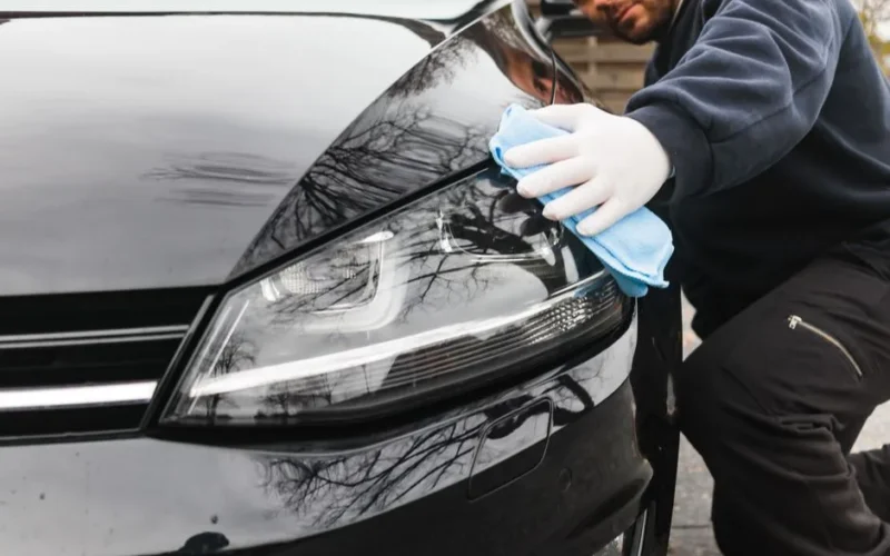 Close-up of a man cleaning a car headlight using a blue cloth outdoors.