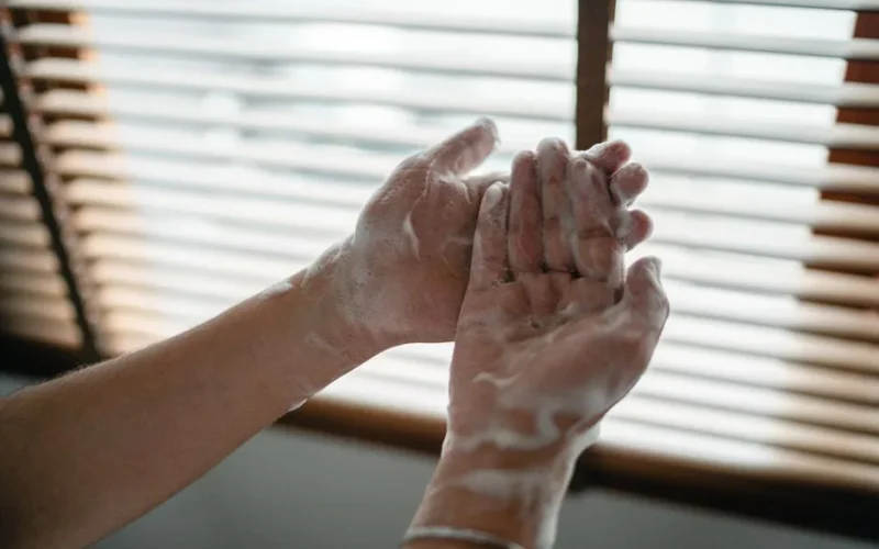 Close-up of adult hands covered in soapy foam against a window light backdrop.
