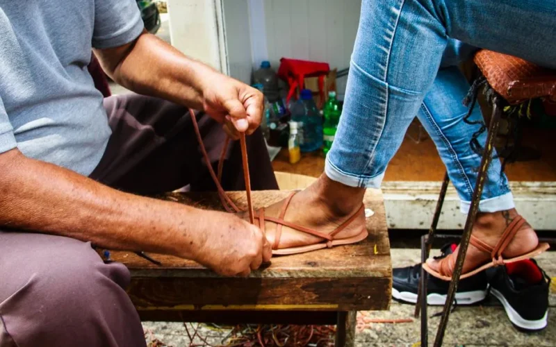 A craftsman skillfully ties leather straps on handmade sandals.