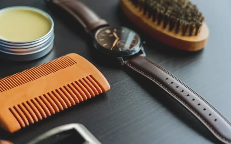 Flat lay image of grooming items with an elegant leather wristwatch on a dark surface.