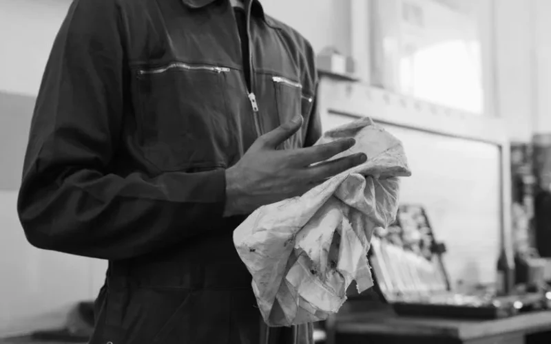Mechanic cleaning hands with cloth in a monochrome automotive workshop setting.