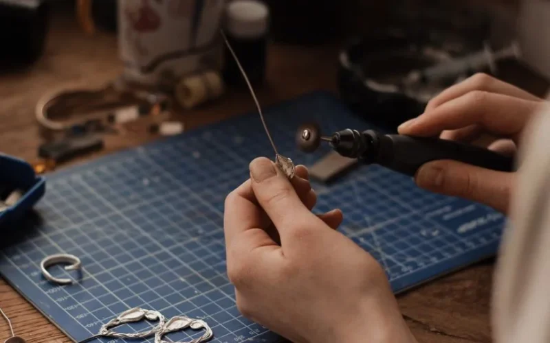Close-up of a jeweler polishing silver earrings at a workbench using precision tools.