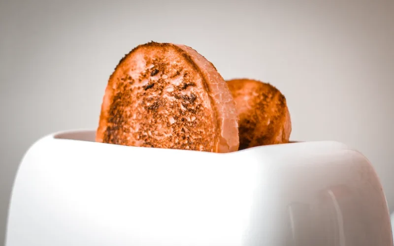 Golden brown slices of bread popping out of a white toaster, ready to serve.