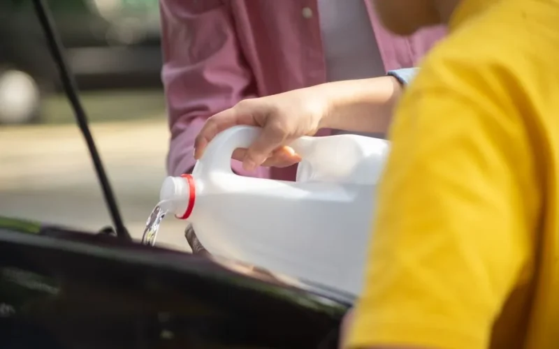 Close-up of hands pouring water into a car engine, focusing on auto maintenance.