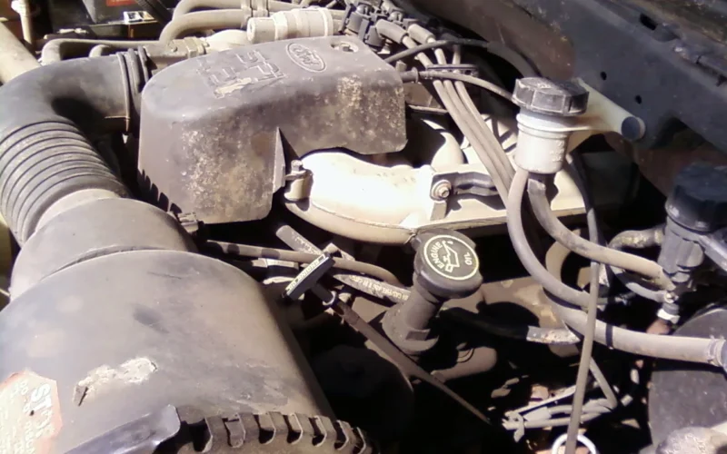 4.2 liter V6 engine installed in a 1998 F-150. Shows the left valve cover (bank 2), the clutch fluid reservoir, air cleaner, throttle body, coil pack, and the master brake cylinder/reservoir.