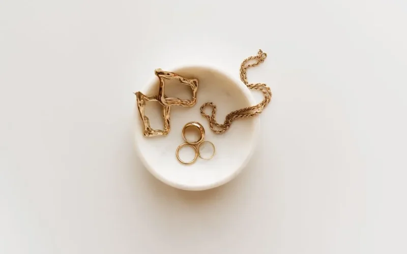 Stylish arrangement of gold jewelry including rings, earrings, and a necklace on a marble dish.