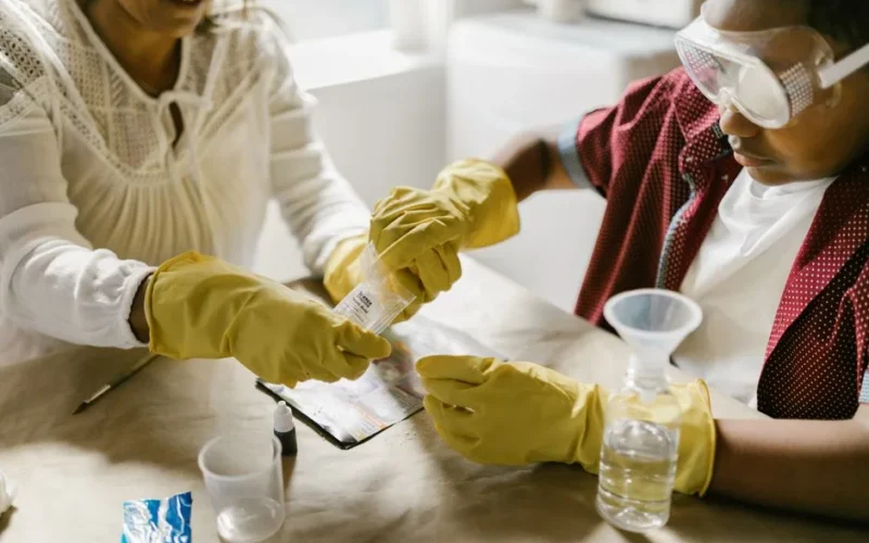 A mother and child conducting a science experiment with gloves and goggles indoors.