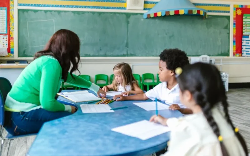 Preschool children engaged in learning with a teacher in a classroom setting.
