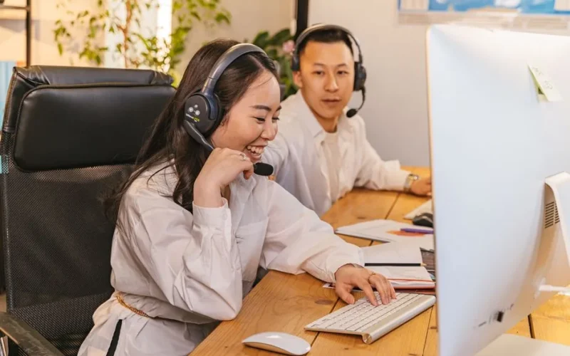 Two call center agents working together, focused and engaged at their desks, communicating via headsets.