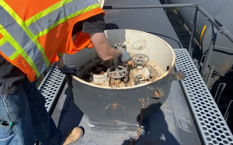 A U.S. Federal Railroad Administration hazardous materials inspector examines inside the protective housing on the top of a tank car, to evaluate the valves inside of the housing to ensure they were in good condition and sealed hand tight, during a Health Hazard Evaluation of railyards in the Midwestern United States. Under NIOSH's Health Hazard Evaluation Program, employees, union officials, or employers can request an evaluation of possible health hazards at their workplace at no cost to them.