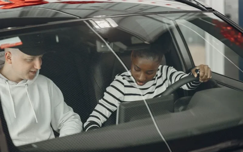 Black woman and caucasian man sitting inside a vehicle, discussing driving.