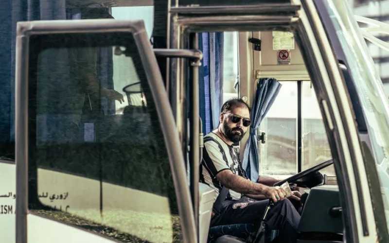 Confident bus driver in sunglasses sits behind the wheel, ready for travel.